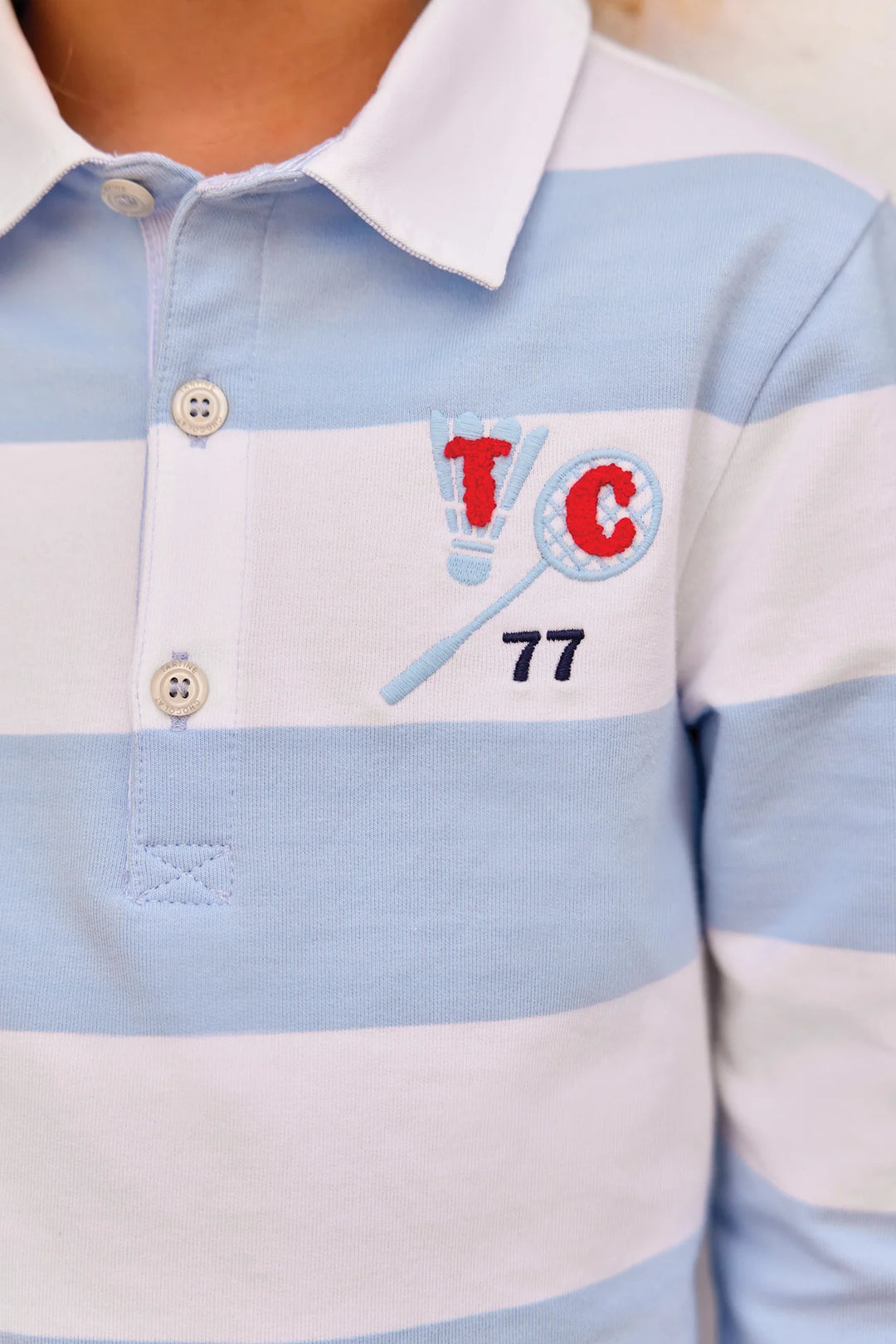 Detail van geborduurde TC badmintonmotief op de lichtblauw-wit gestreepte baby polo van tartine et Chocolat 