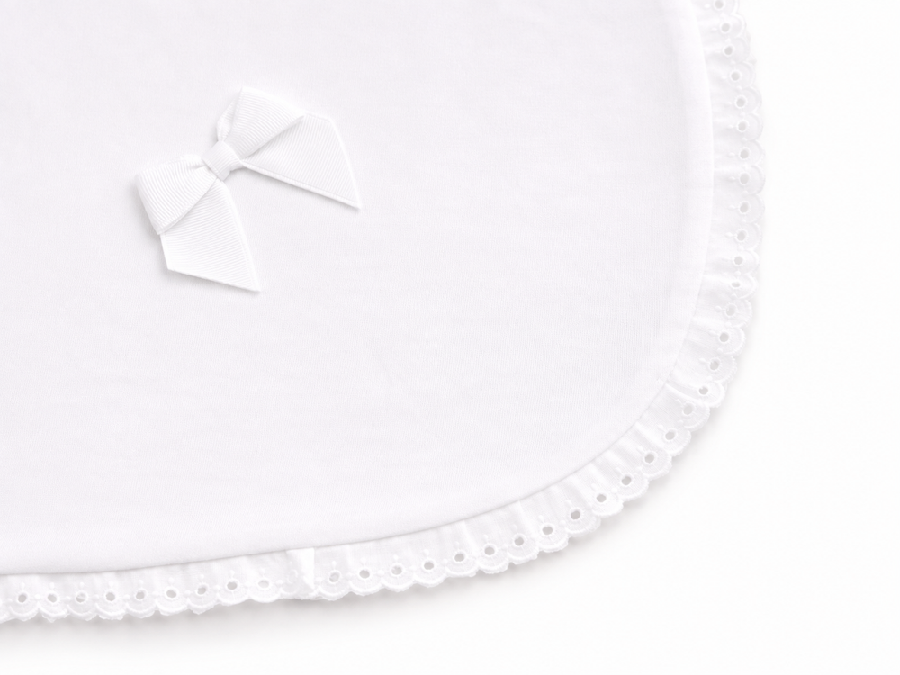 detail van witte velours deken met broderie rand en grograin strik